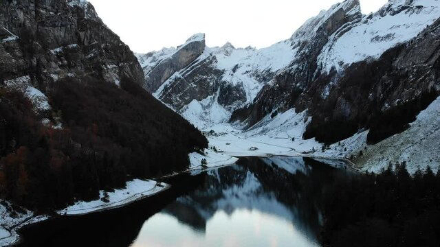 Aerial flyover across Seealpsee in Appenzell, Switzerland in winter towards the peaks of Alpstein and their reflection  - 4k