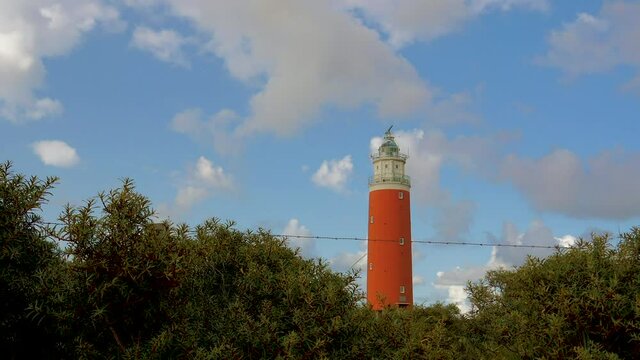 Time Lapse of a wide angle steady shot of sea ​​buckthorn in the foreground. In the background a lighthouse in the dunes. The sky is blue with beautiful clouds passing by.