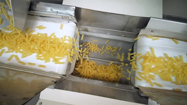 Two white conveyor belts move raw spiral shaped pasta to another one wave shaped conveyor belt that divide a macaronis on equal portions before packing