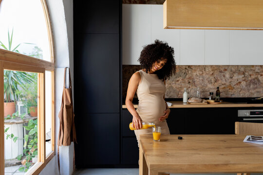 Pregnant serving herself orange juice at kitchen