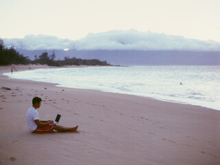 Young man on the beach shore checking emails and forecast before surfing