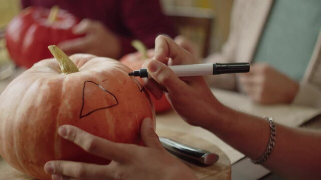 A man draws on a pumpkin with a marker and carefully examines the lamp