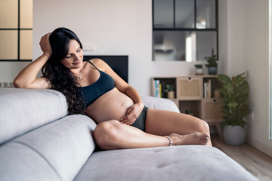 Smiling pregnant woman touching her belly and looking at it with