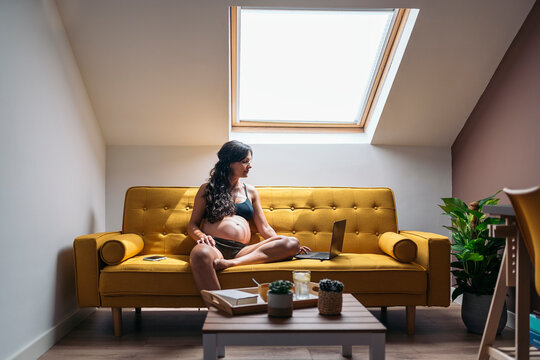 Relaxed pregnant woman browsing on the internet on a laptop whil