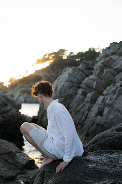 Stylish Man Sitting On Rocks Looking At The Sea