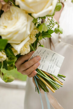 Bride's hand with bouquet and wedding vow on paper