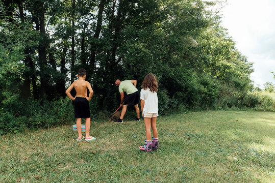 Two kids watching dad dig a hole. 