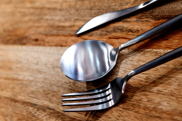A high-angle view of a spoon and fork placed on a wooden table with a place to copy.