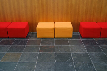 Red and yellow cube shaped seat cushions on a slate tile floor with a wood panel wall behind
