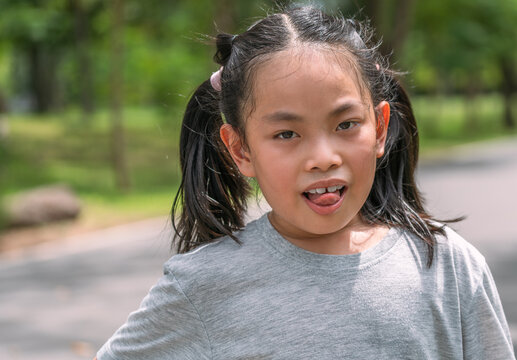 Portrait Asian child girl in the park, many sweats on the face,  tongue out to show tired, gray color t-shirt, blurred background of trees in the park, sunlight image.