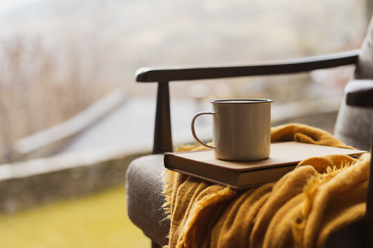 Detail of coffe cup and book on top of chair by window