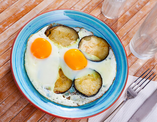 Plate with appetizing fried eggs, cooked with sliced and roasted eggplant