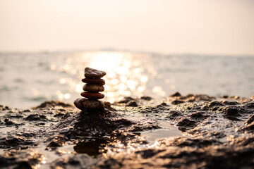 Pyramid pebble on stone with sun set on sea nature at coast. stack zen with ocean bokeh twilight landscape background. balance, stability, calm, relax, aroma therapy spa symbols concept.