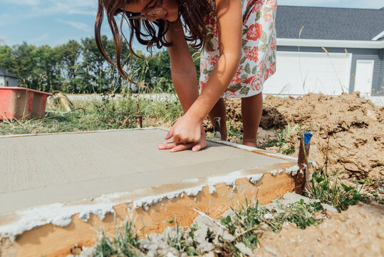 Girl pressing hard on concrete to make print. 