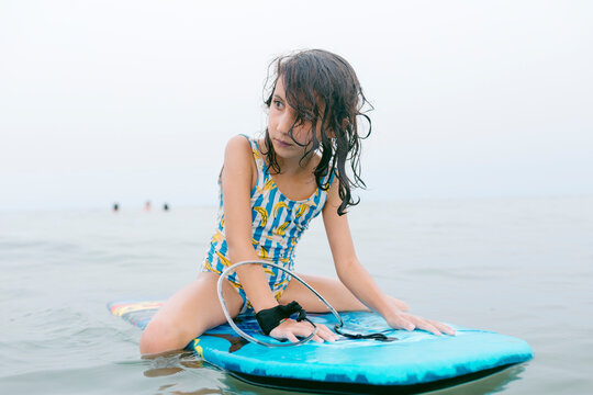 Kid with wet and long hair sitting on bodyboard