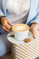 Close-up of female hands in blue suit holding a cup of cappuccino