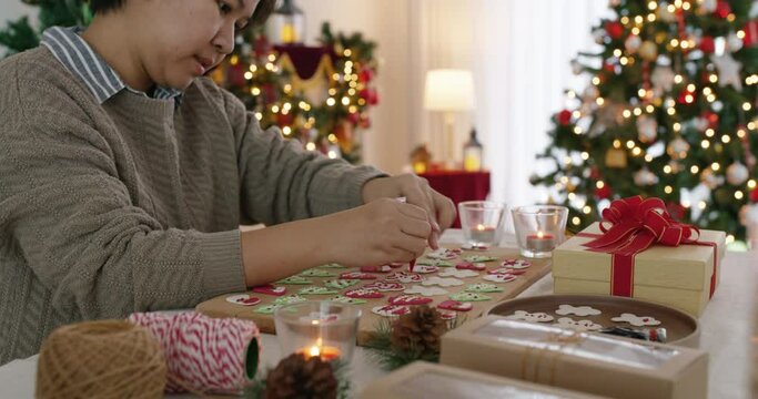 Asia happy adult people woman enjoy make craft gift for Xmas eve party snack cooking food recipe on kitchen table in good warm time. Cute smile gingerman bakery icing sugar with red green white color.