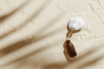Serum or Liquid Collagen dropper bottle on sand background with sunlight, shadow ftom palm leaves, natural round stone