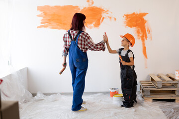 Mom and her little son are doing repairs in the room, they painted the wall orange with a brush and...