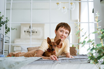 Cute woman lying on her stomach relaxing in bed with her beloved dog. Morning caresses in a warm comfortable bed. Cute woman and her dog are sleeping in bed,