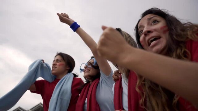 Group of female fans enthusiastically celebrating their team's victory in the sporting event. Women enjoying the sport in the stands of the stadium.