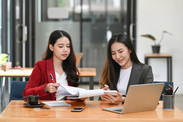 Two businesswoman colleagues sitting in office and analyzing financial documents together.