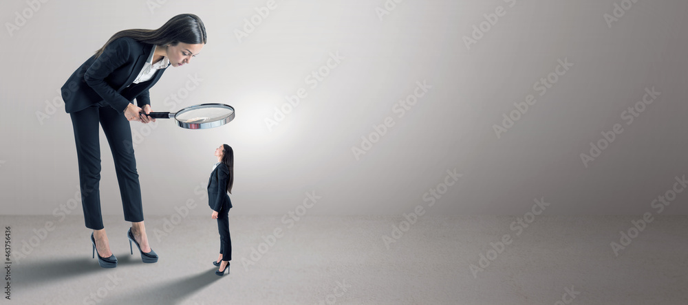 Poster Female in suit using magnifier magnifying glass to look at tiny subordinate on concrete background with shadow and mock up place. Hiring and dominance concept.