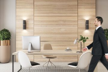 Attractive young european businessman stading in modern office interior with desktop, equipment and...