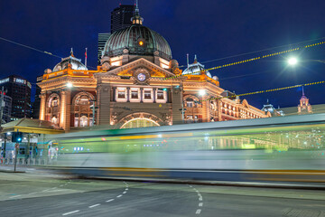 Melbourne, Victoria, Australia - 2021: Melbourne's iconic, Flinders St Station facade, with passing tram at dusk. - obrazy, fototapety, plakaty