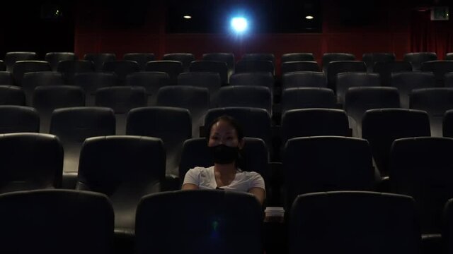 Front View Of A Korean Woman Sitting Alone In The Dark Cinema And Watching Movie After A Long Day with Nobody Around during Covid-19 Coronavirus Pandemic in South Korea wide