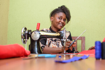 An African female tailor, fashion designer or dress maker, making stylish and fashionable clothes with sewing machine in a tailoring workshop