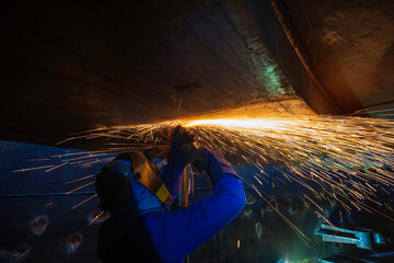 Male worker  grinding on steel plate with flash of sparks close up wear protective gloves