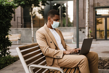 Young black man working with laptop while sitting on bench