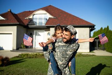 Portrait of father soldier in uniform on military leave holding his lovely daughter in front of their house. - obrazy, fototapety, plakaty