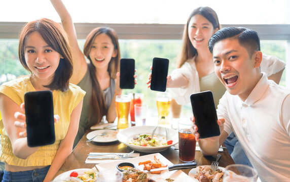 Happy Young Group Showing Mobile Phone With Blank Screen In Restaurant