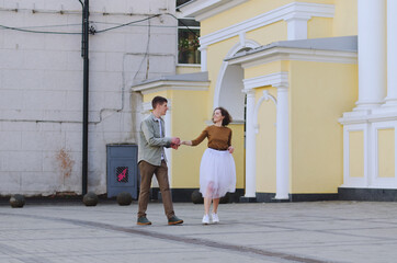 Love story of stylish funny couple: young man in a t-shirt. And a cute young woman in wedding white skirt and yellow sweater. Family holiday and togetherness, date.