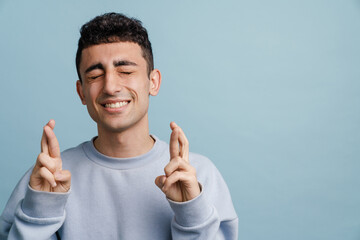 Young middle eastern man holding fingers crossed for good luck