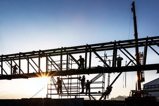 Construction workers are working on structure steel at sunset. A construction worker is a worker employed in manual labour of the physical construction of the built environment and its infrastructure.