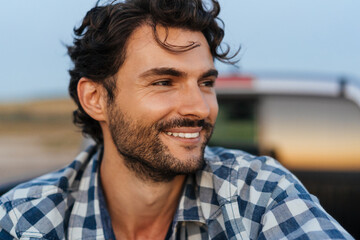 Young white man smiling at camera while sitting in trunk