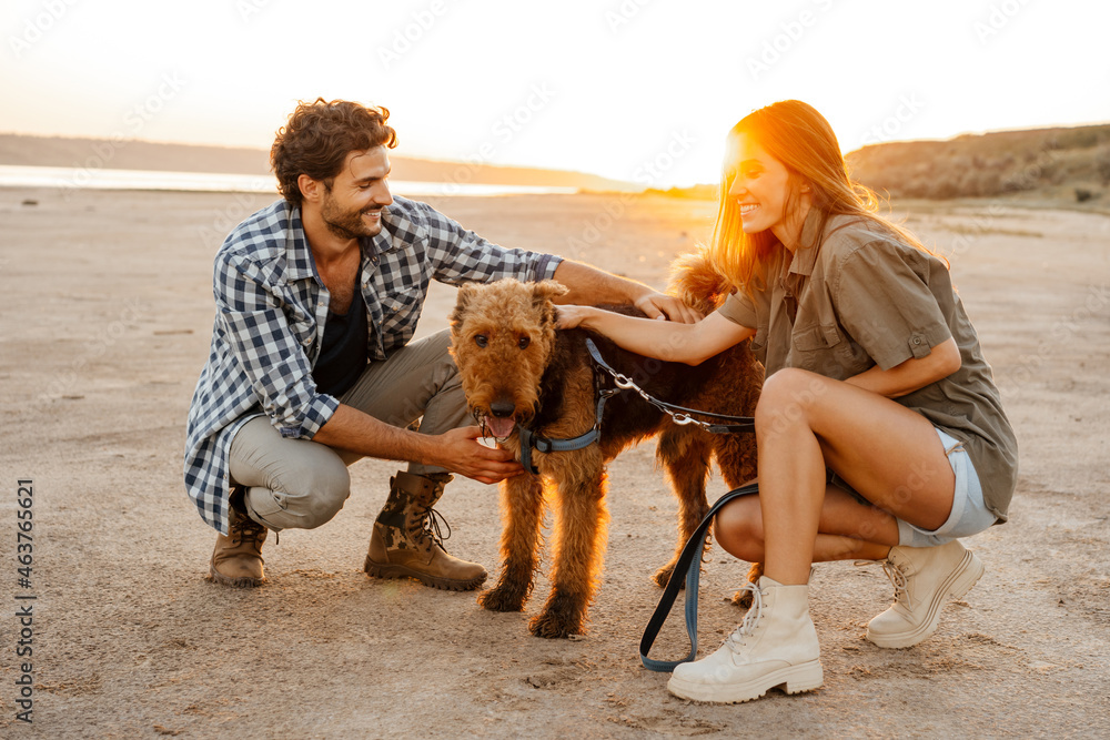 Wall mural White young couple smiling and stroking their dog while walking together