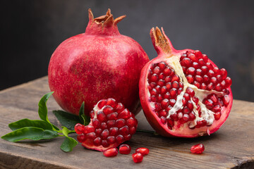 Healthy pomegranate fruit with leaves and half of ripe pomegranate on a cutting board, side view, dark vintage background.