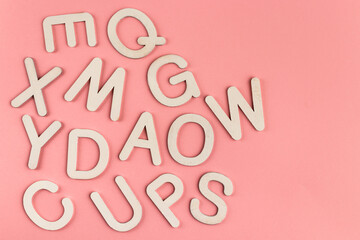 Wooden alphabet letters on pink paper background.