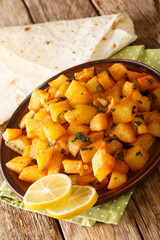 Batata harra is a Lebanese vegetable dish it consists of potatoes, paprika, coriander, chili, and garlic which are all fried together in olive oil close up in the plate on the table. Vertical