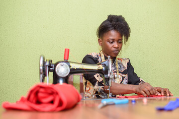 An African female tailor, fashion designer or dress maker, making stylish and fashionable clothes with sewing machine in a tailoring workshop