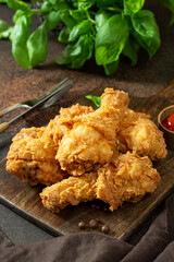 Fried crispy chicken legs in breadcrumbs on a wooden serving board on a dark background. Fast food from the drumstick close-up	