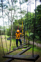 An Asian kid walking confidently and carefully through wooden boards hanged by safety ropes.