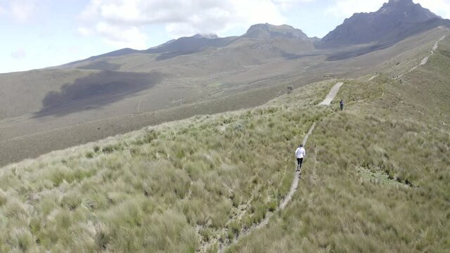 A woman is running on the moorlands of the Andes in a trail close to Rucu Pichincha near Quito, Ecuador. Grass, mountains and vegetation are seen in the altitudes.