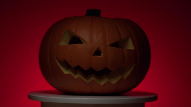 halloween orange smiling pumpkin with carved teeth, eyes and nose, dynamic light, on a rotating circular light platform in red light on a dark background