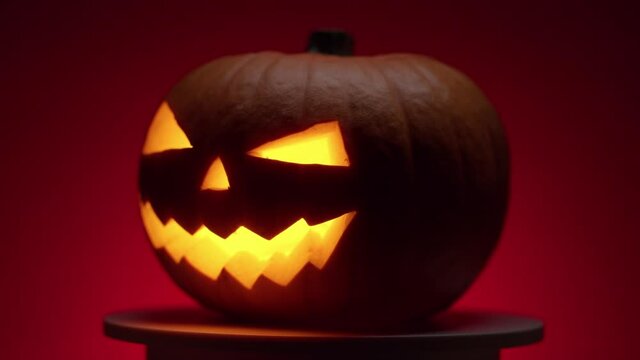 continuous looping rotation of a halloween pumpkin with carved teeth, eyes and nose, with a glowing fanar inside in the dark on a red background