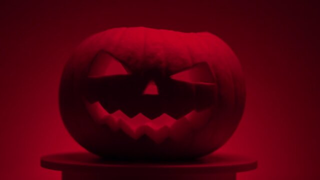 continuous looping halloween pumpkin with carved teeth, eyes and nose on a rotating round light platform on a dark red background